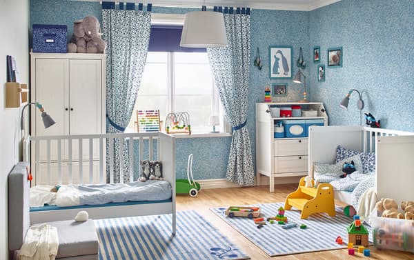 A blue themed baby bedroom with two IKEA SUNDVIK white cots, an IKEA SUNDVIK changing table and a white wardrobe.
