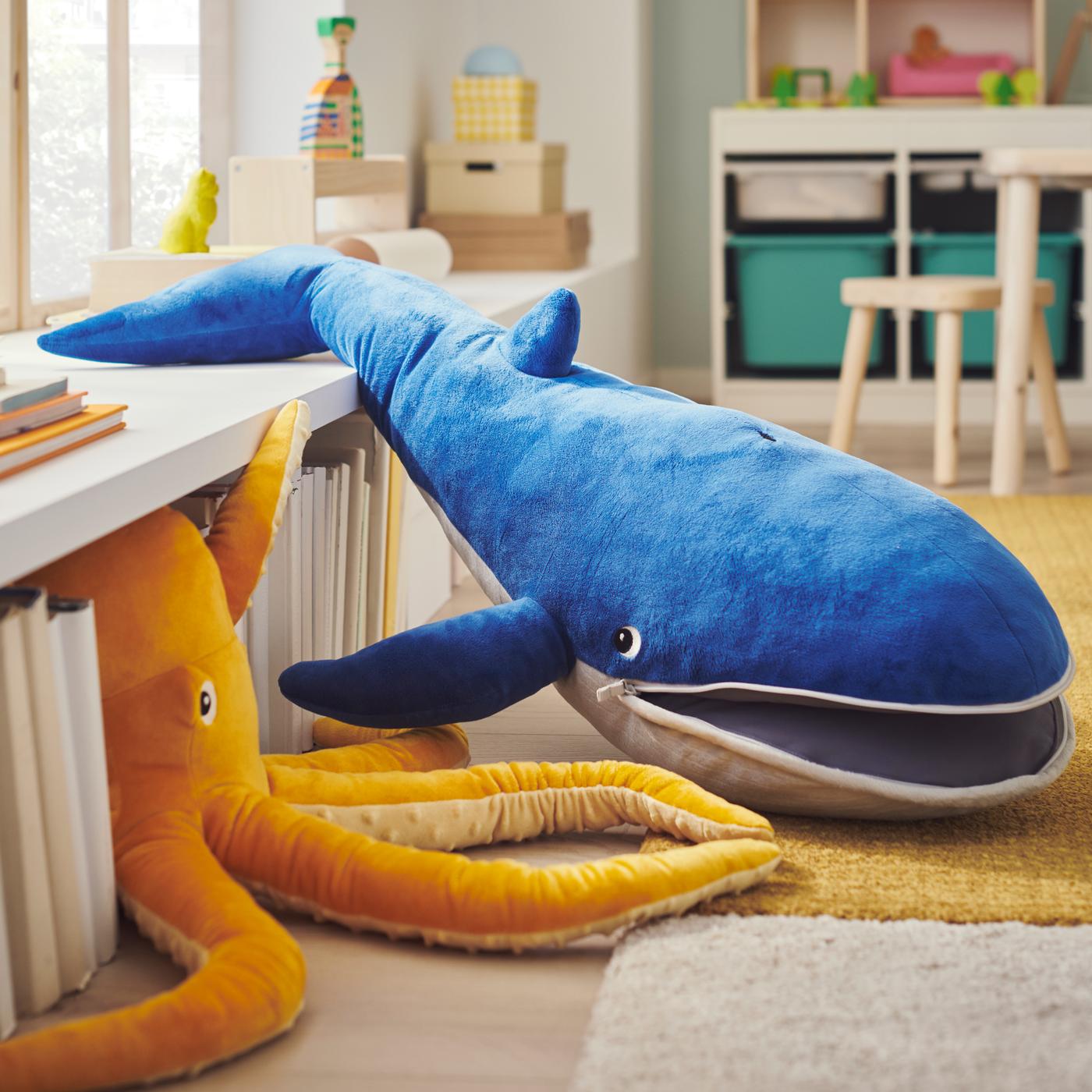 A blue whale and a yellow octopus BLÅVINGAD soft toy extend between a yellow low pile LANGSTED rug and a white cabinet.