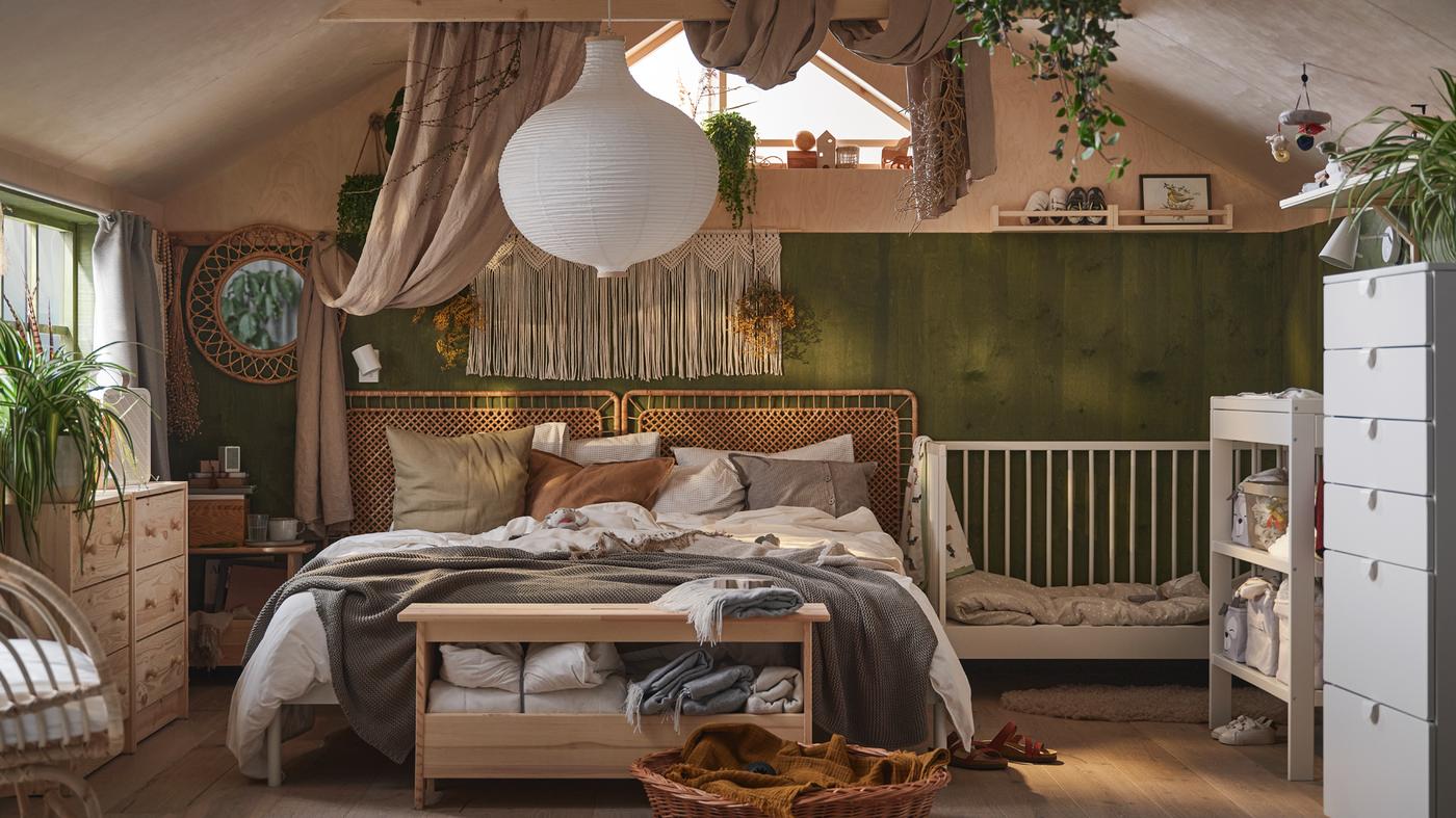 A boho feel bedroom with a double bed draped in neutral bed linen and cushions, and a white GULLIVER cot beside it.