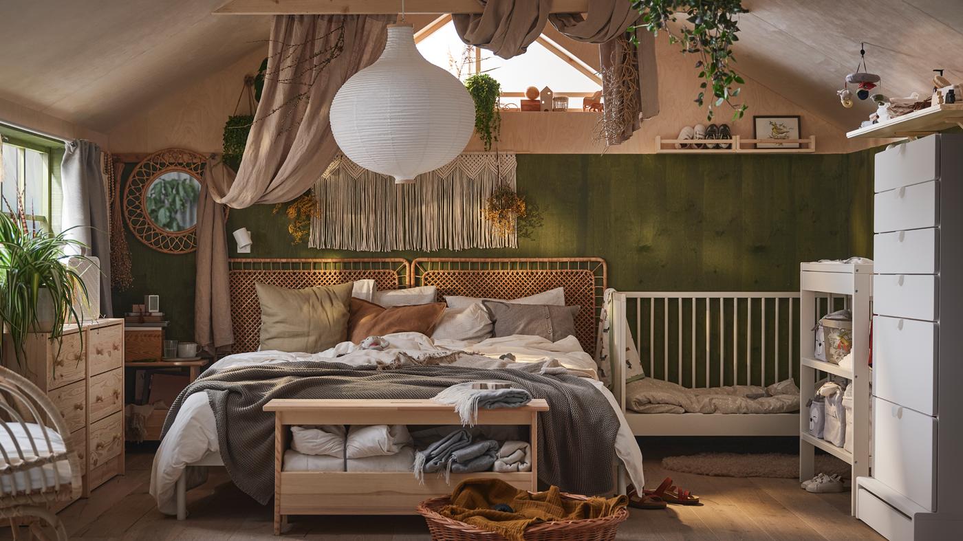A boho feel bedroom with a double bed draped in neutral bed linen and cushions, and a white GULLIVER cot beside it.