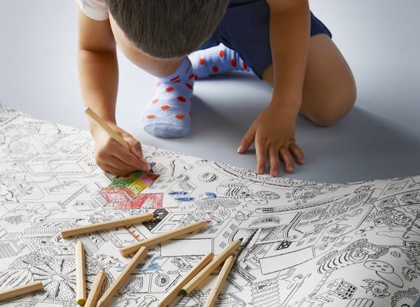 A boy colouring black-and-white drawings on a LUSTIGT colouring paper roll with MÅLA coloured pencils.