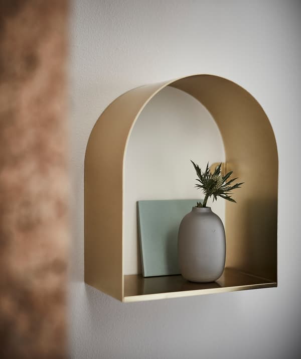 A brass coloured TOSSÅSEN display shelf with a vase and flower.