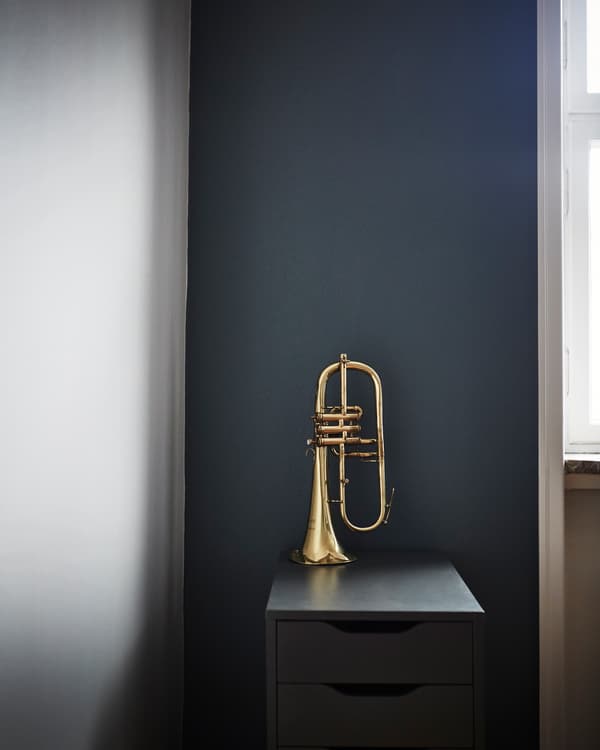 A brass trumpet sits on a drawer unit in front of a dark wall.