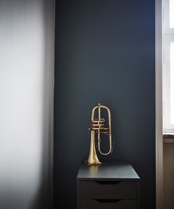 A brass trumpet sits on a drawer unit in front of a dark wall.