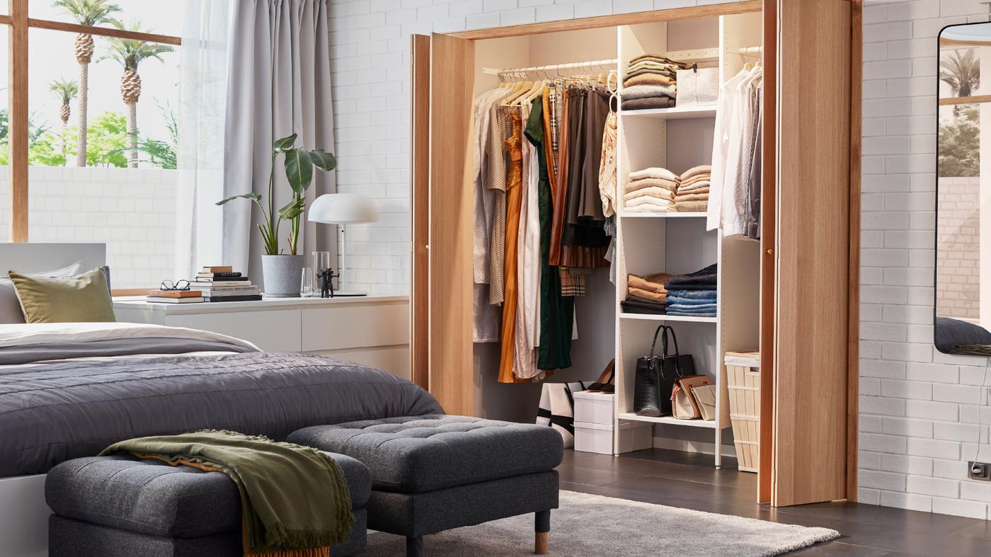 A bright bedroom with a fitted AURDAL wardrobe, a white MALM bed with grey bedding and two dark grey MORABO footstools.