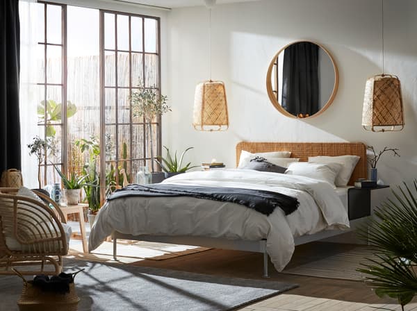 A bright bedroom with lots of natural materials, like rattan and bamboo. Big glass doors and an outdoor area next to the bed.