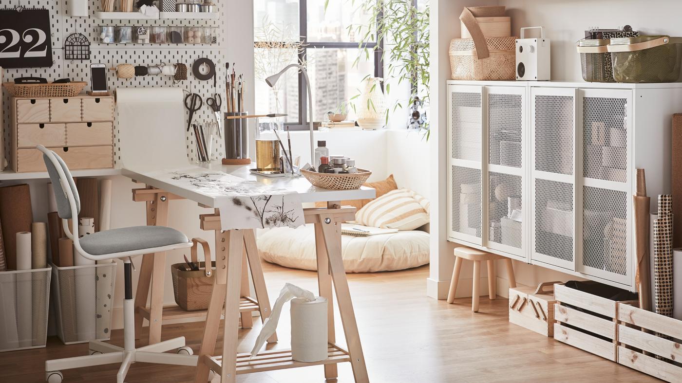 A bright home office with a white desk, a white/yellow green swivel chair and a white pegboard with crafting materials.