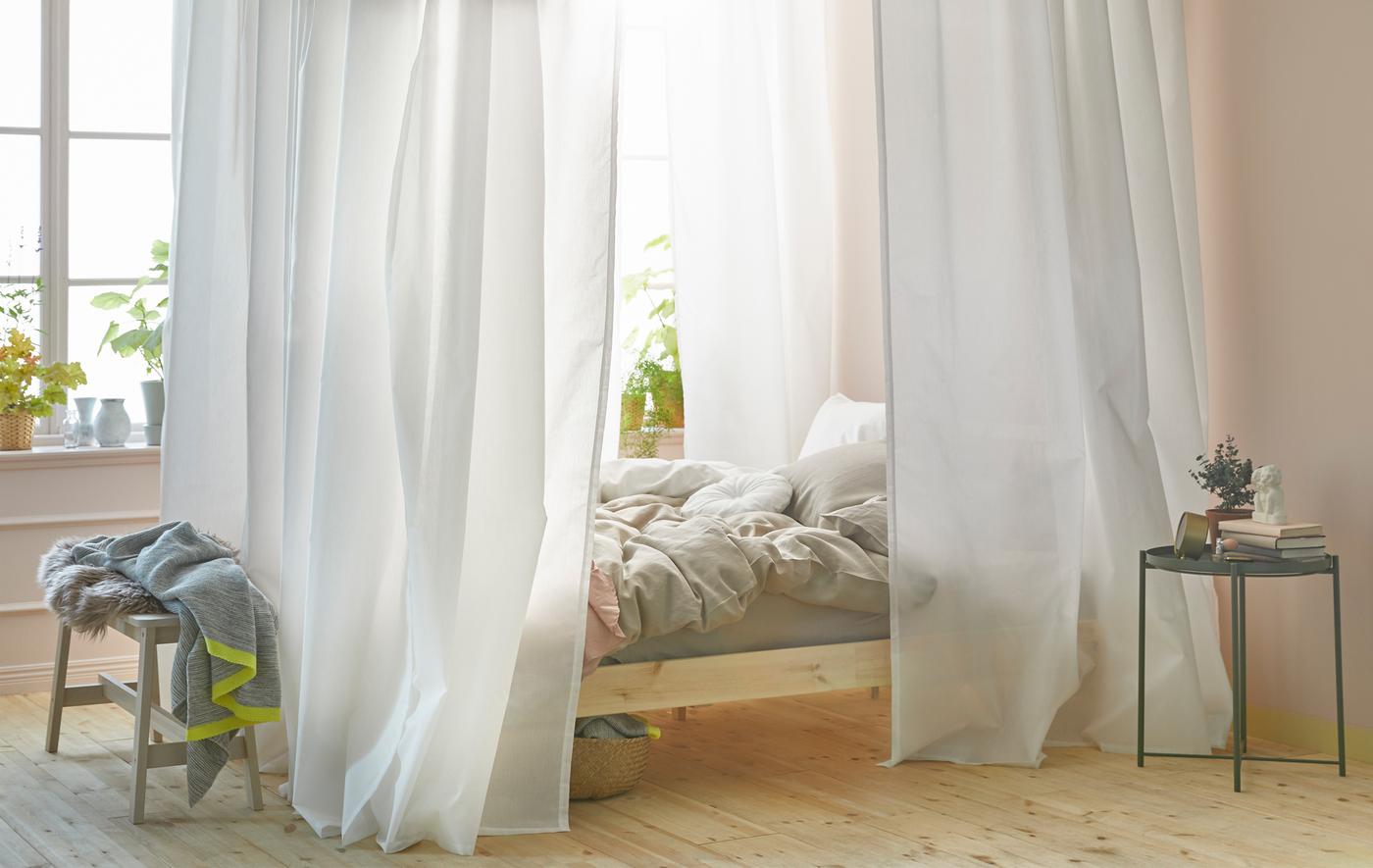 A bright, light bedroom with a canopy bed made with white curtains and the IKEA VIDGA track system.