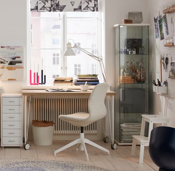 A bright workspace with a white desk, desk chair, storage cabinet and organized storage around.