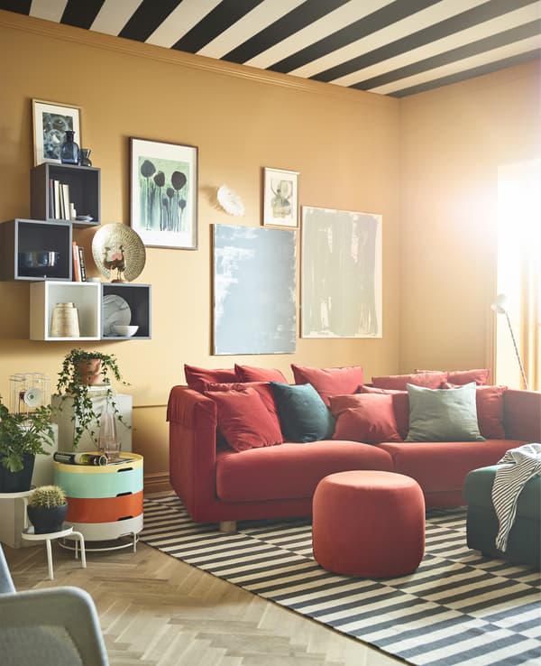 A brightly coloured living room with ochre walls is burnished with a red sofa and ottomans.