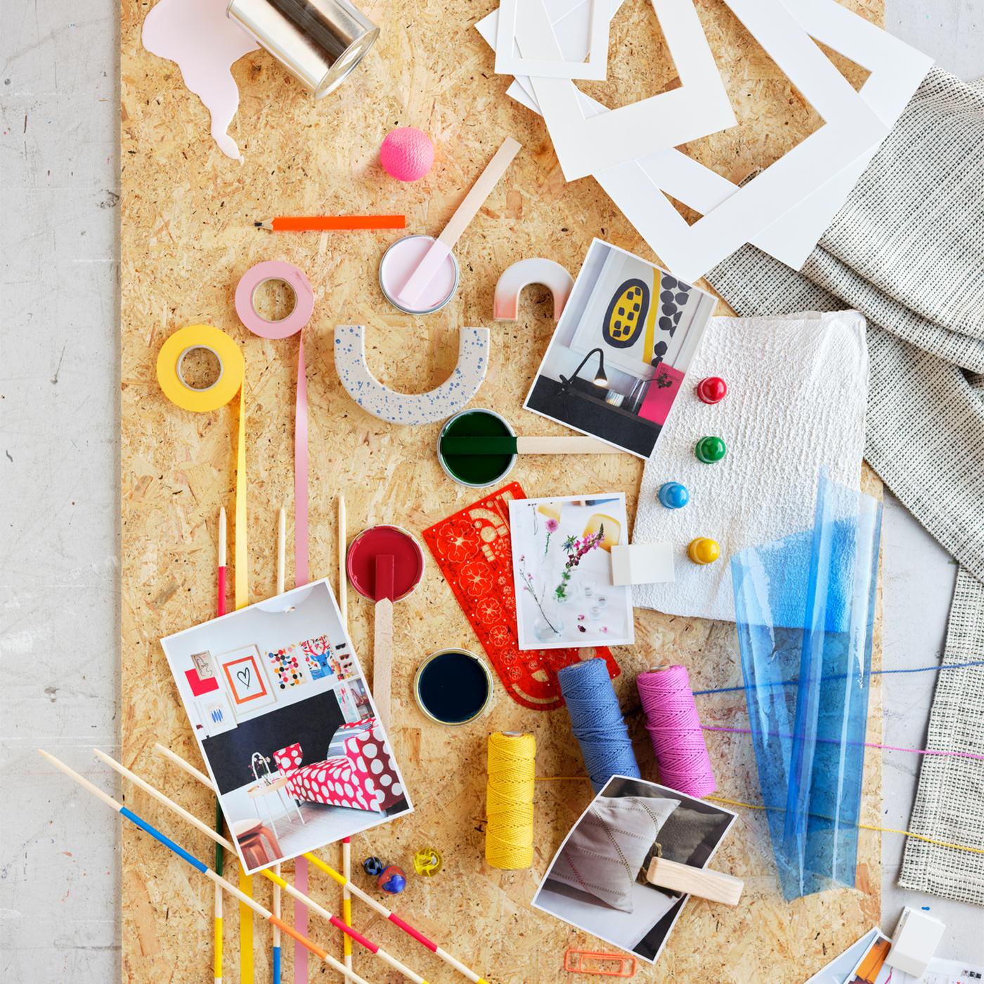 A brightly coloured mood board with washi tapes, spools of thread, white cardboard frames and photographs.