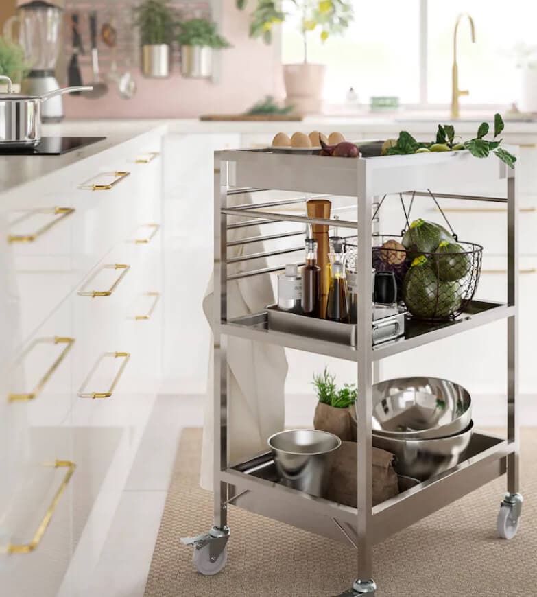 A brightly lit pink kitchen with a metal trolley with bowls and other acessories.