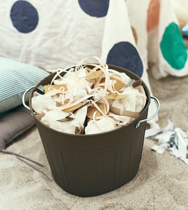 A bucket full of packet-up food sits in the sand.