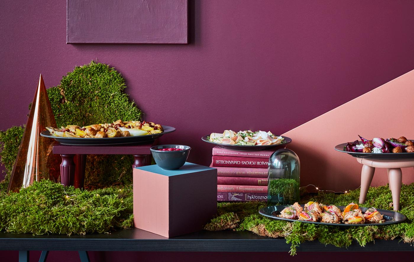 A buffet table is set with food, greenery, and decorations in shades of dark red and green.