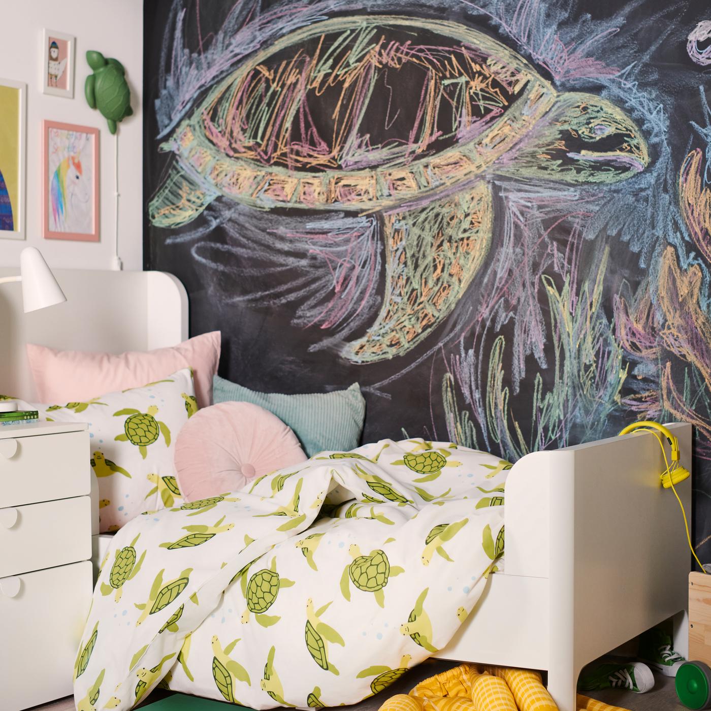 A BUSUNGE bed is dressed in a BLÅVINGAD green turtle duvet cover with cushions in front of a chalkboard wall.
