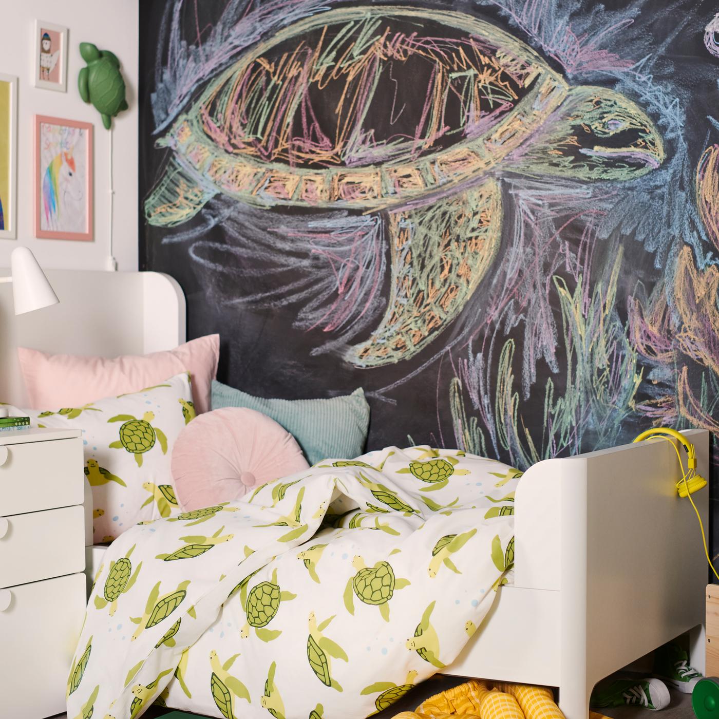 A BUSUNGE bed is dressed in a BLÅVINGAD green turtle duvet cover with cushions in front of a chalkboard wall.