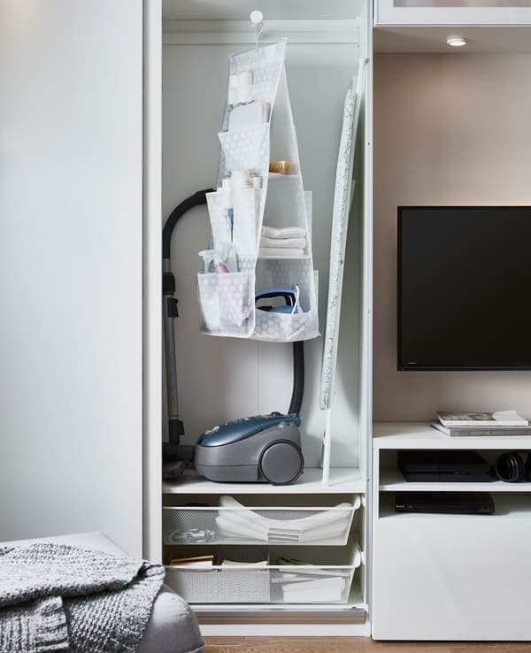A cabinet stores cleaning and clothing care items like a vacuum cleaner, iron and ironing board.