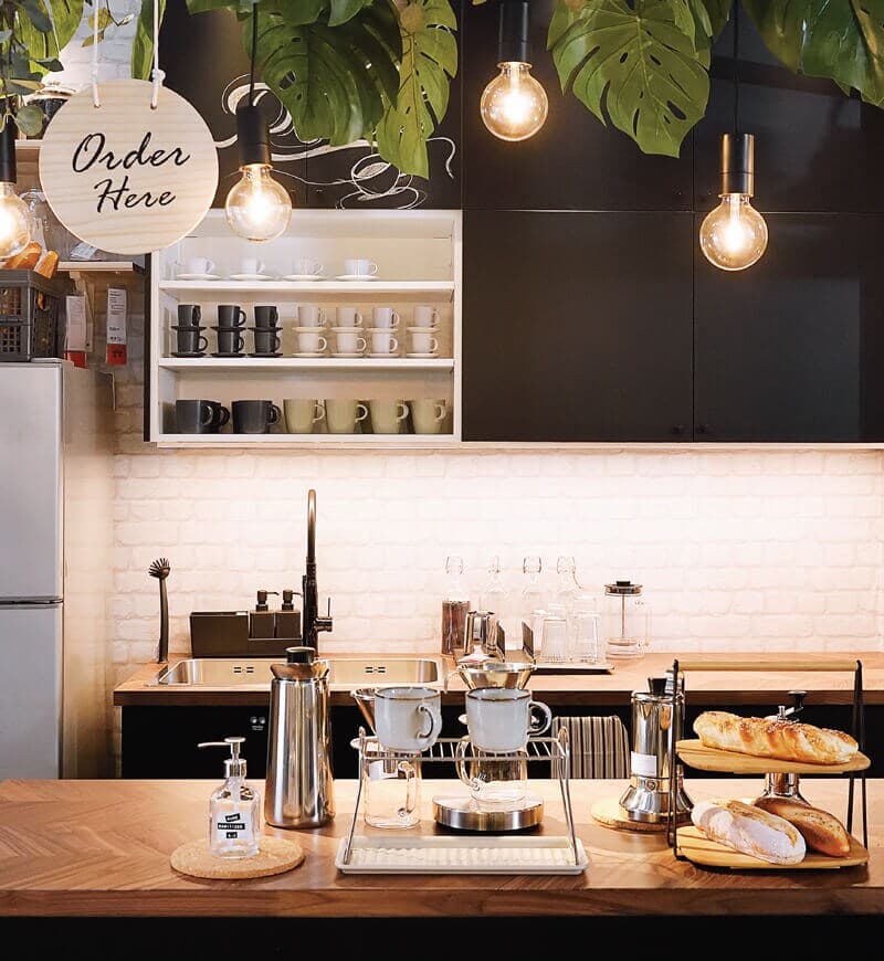 A café ordering area featuring two wooden countertops with coffee-making accessories and plants at the top of the ceiling.