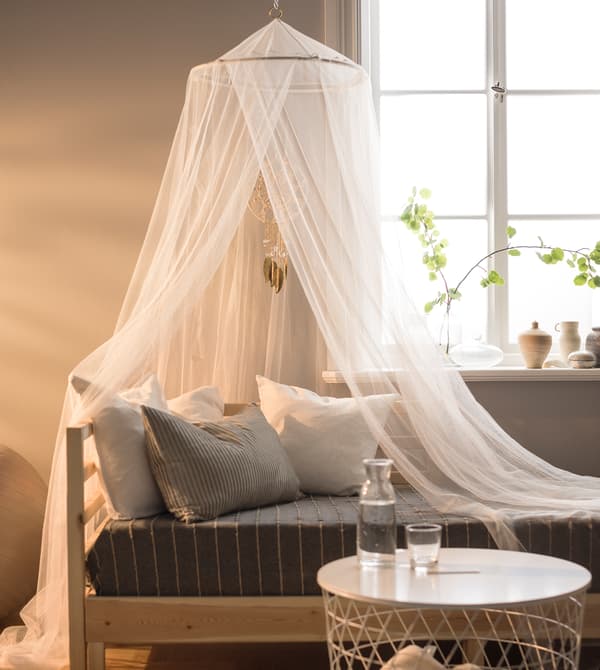A canopy and a day bed sit in front of a window.