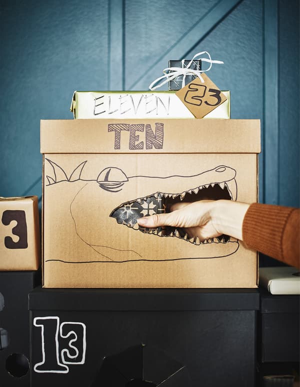 A cardboard box with a crocodile drawn on it and a hand reaching in the mouth for a gift.
