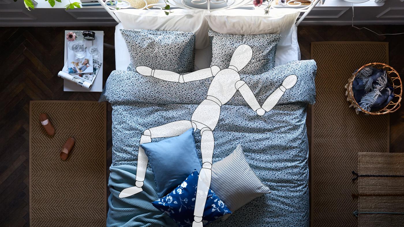A cartoon drawing of a person is asleep on a LEIRVIK bed with VATTENMYNTA bed linen. On each side of the bed is a brown rug.