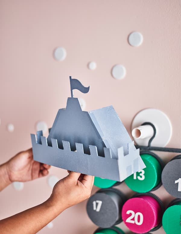 A castle top made from paper being attached to a hanging advent calendar.