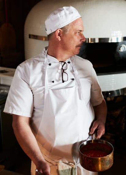 A chef in white clothing is holding a frying pan and looking to the left.