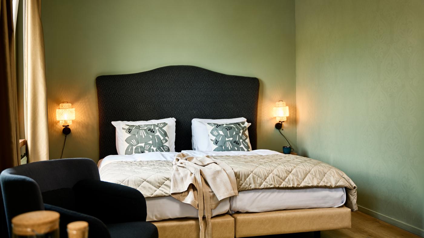 A chic bed in a hotel room with fresh green walls