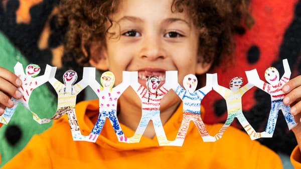 A child in an orange sweater is holding coloured paper garlands that look like children holding hands.