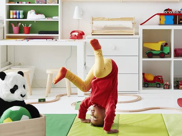 A child in red rolling on a play mat in a child care with many toys on display shelves.