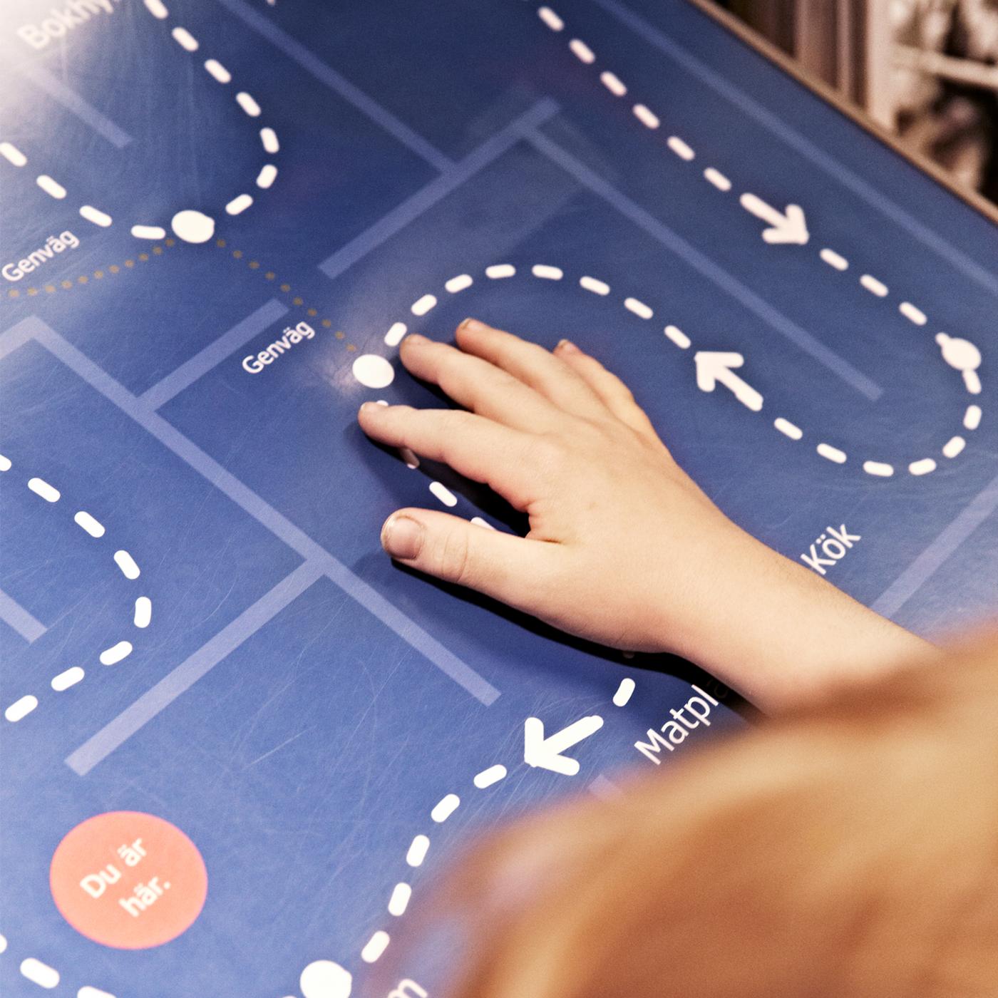 A child stands in front of a floor plan of an IKEA store with one hand following a dotted line on the plan.