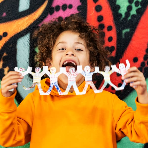 A child with an orange sweater holds a playful garland in front of a colourful wall.