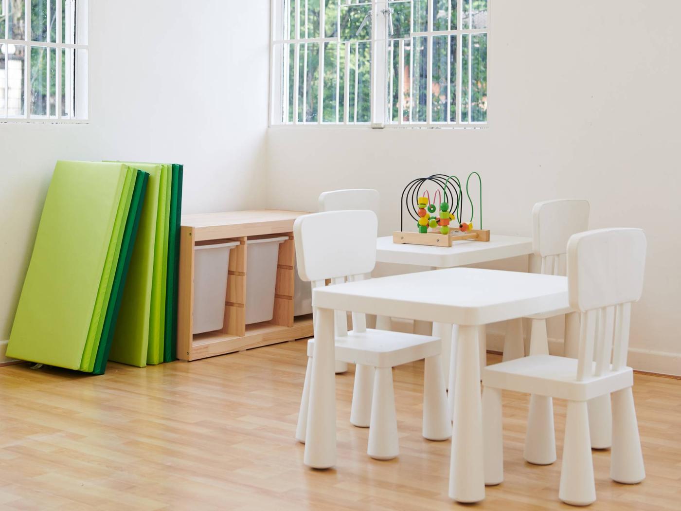 A children classroom featuring a white tables and chairs, playmats and toys.