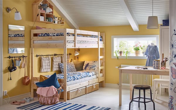 A children’s bedroom with an IKEA MYDAL bunk bed in pine, a work desk, a NÄPEN white clothes stand and stools.
