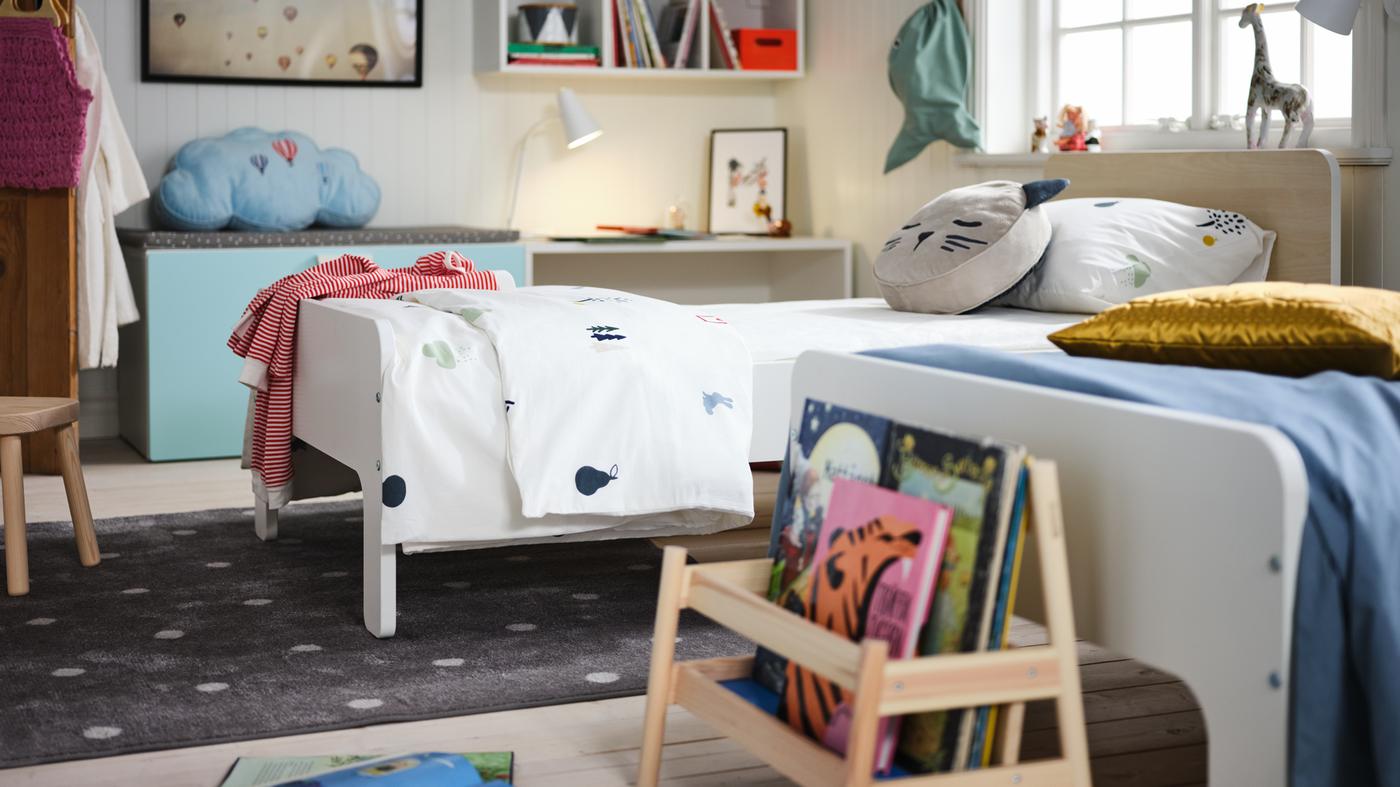 A children’s room with a pair of side-by-side, white SLÄKT extendable beds. Toys, decorations and storage dot the room.