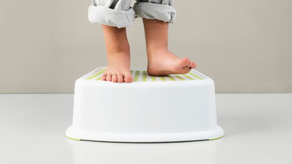 A child's bare feet standing on a plastic stool with their pants rolled up past their ankles. 