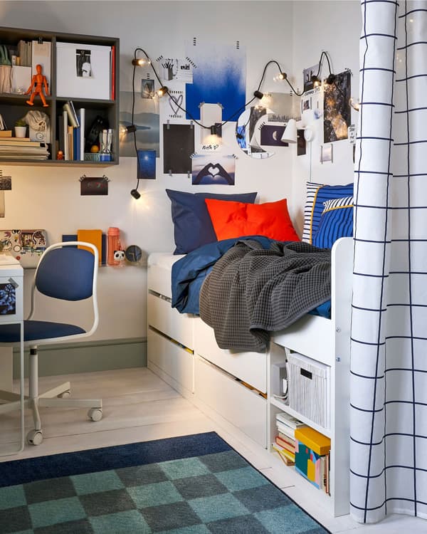 A child’s bedroom with a single bed and under-bed storage, wall-mounted storage and a privacy curtain.