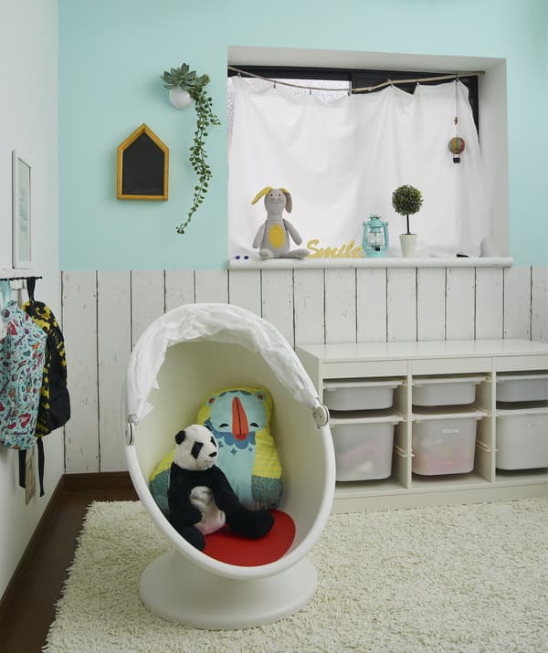 A child’s playroom with storage boxes and soft toys in a child’s armchair on a rug.