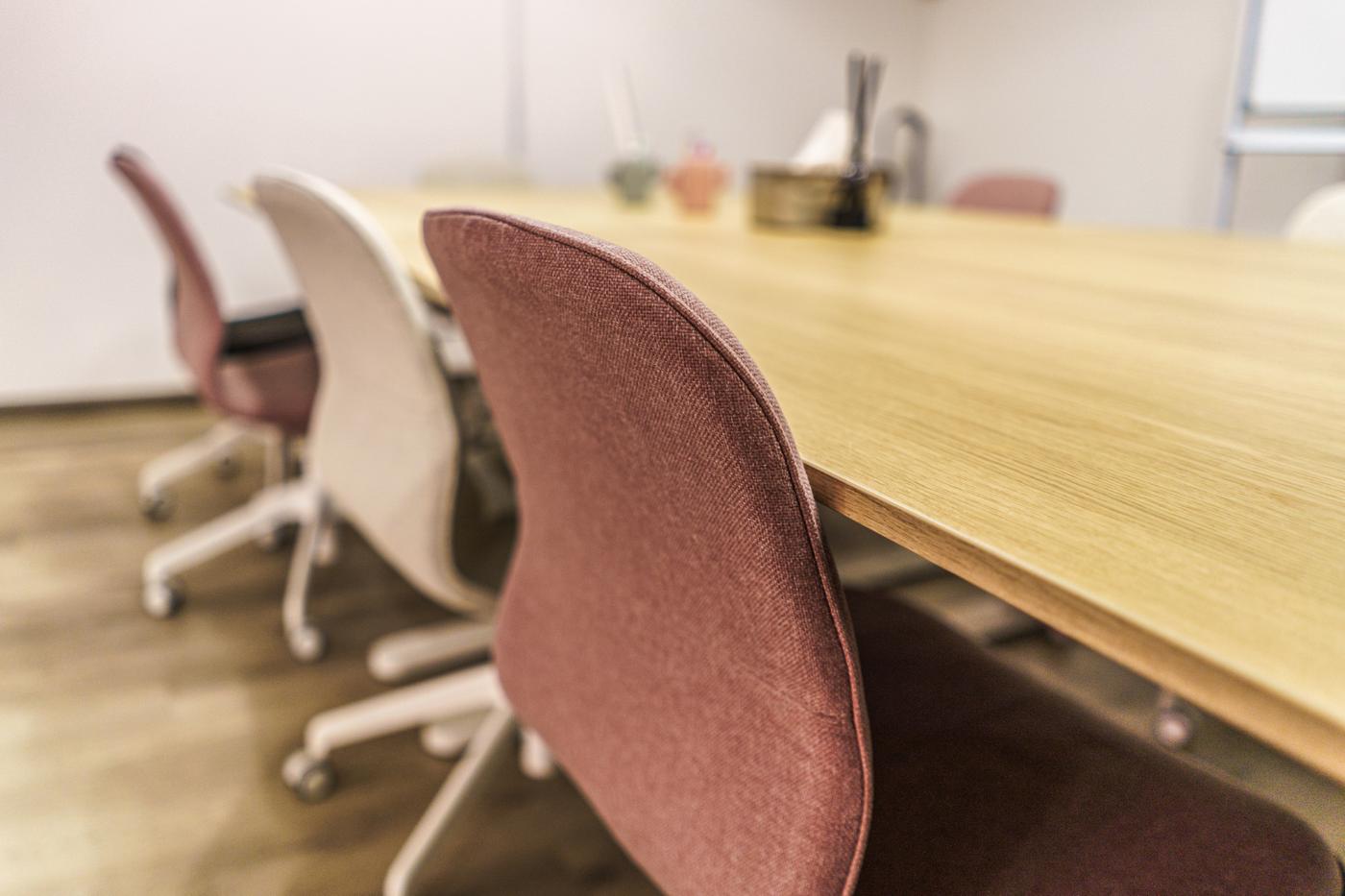 A classroom space featuring a wooden table and white and maroon swivel chairs.