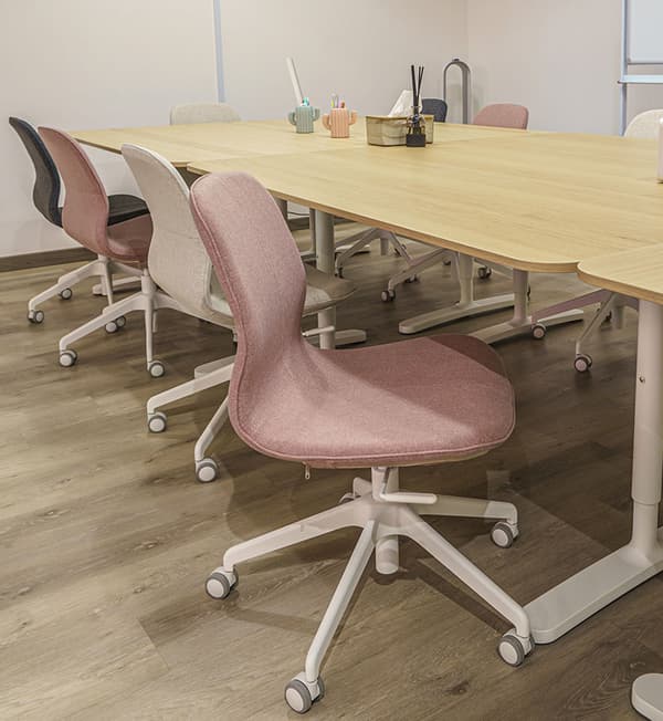 A classroom space featuring wooden desks and swivel chairs of various colours.