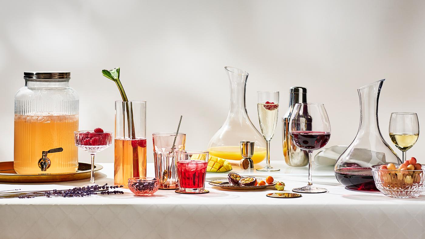 A clear glass carafe and different drinks in various wine glasses and drinking glasses on a table with a white tablecloth.