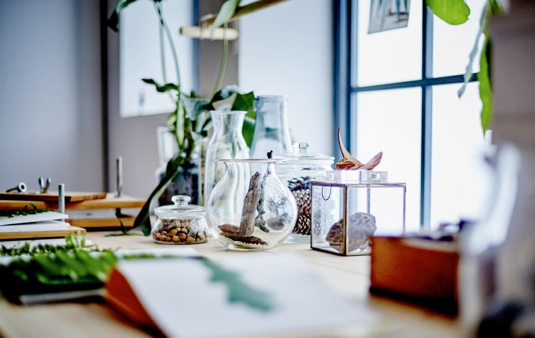 A close-up image of a desk in front of a window, decorated with botanical elements.