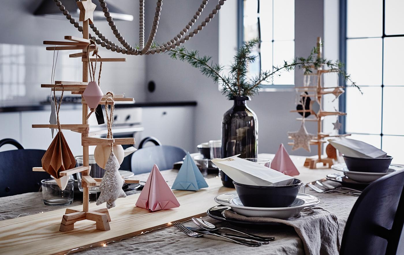 A close-up image of a dining table decorated with pastel origami, greenery in a vase and a wooden board down the center of the table.