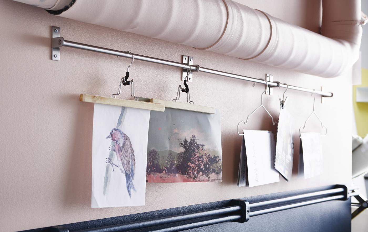 A close-up image of artwork hung with hanger from a rail mounted between pipes.