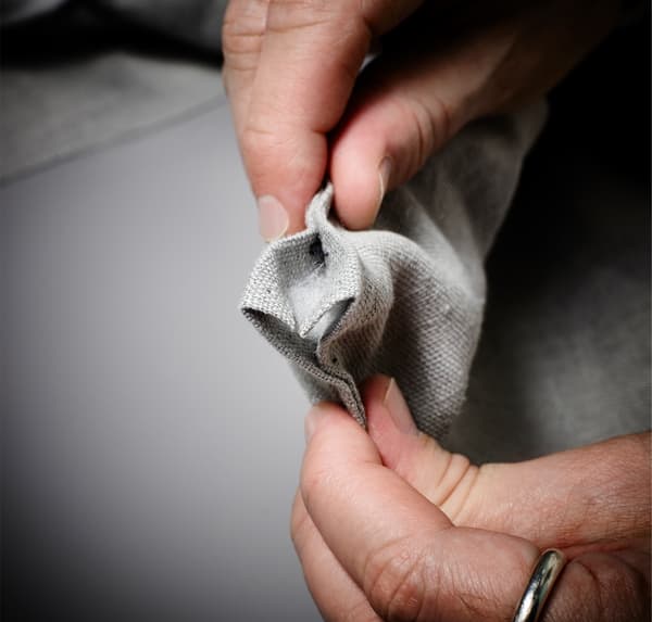 A close up image of hands, showing how to pin the hem in place on grey fabric.