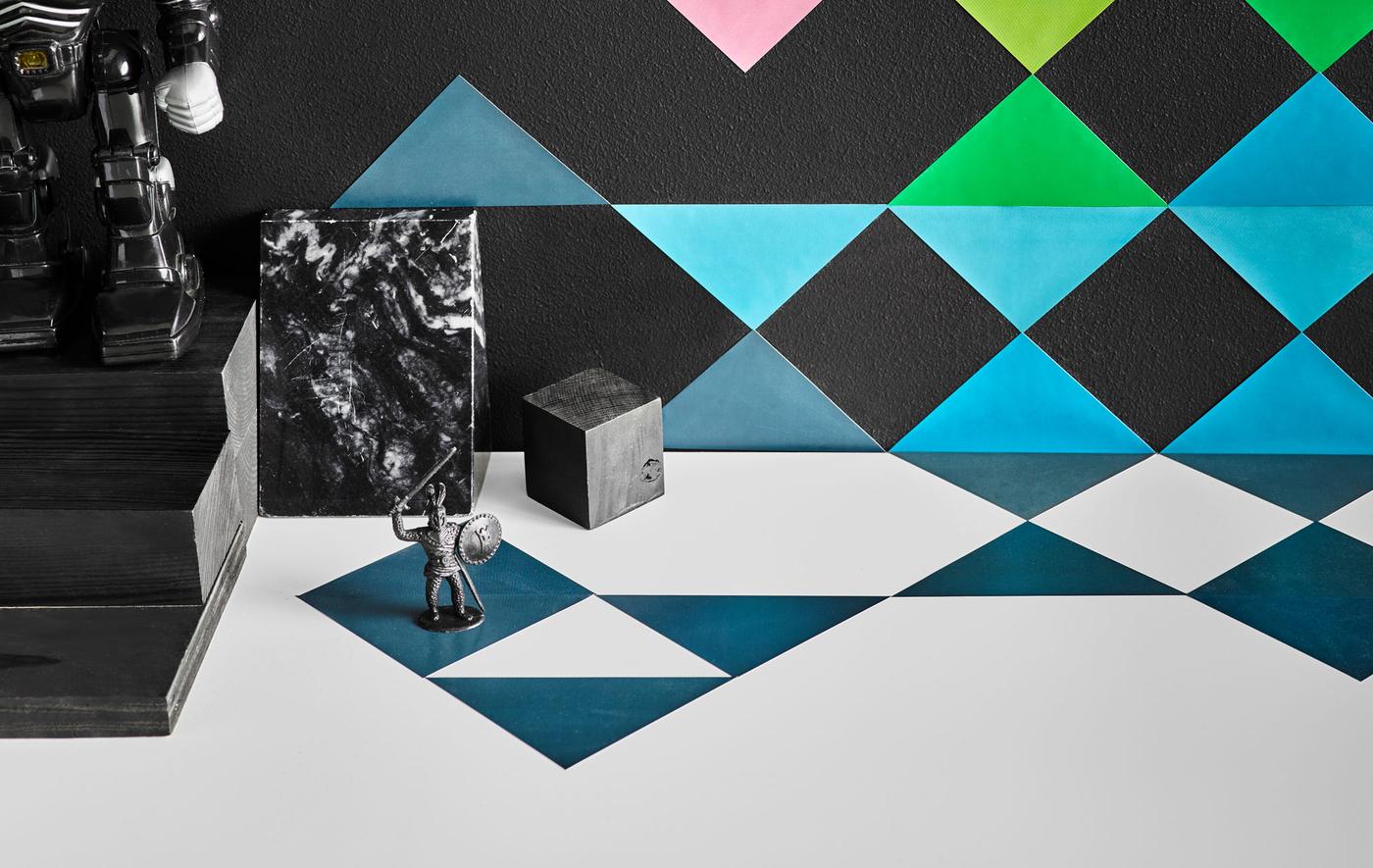 A close up image of multi-coloured triangular stickers arranged decoratively on a wall and a kid’s desk.