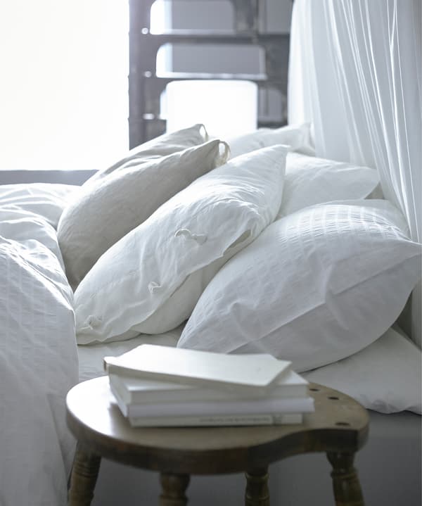 A close-up image of white pillows lying on a bed and with some white books on the bedside table.