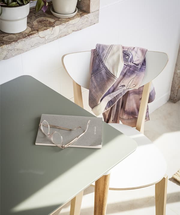 A close-up of a grey table and white chair bathed in sunlight.
