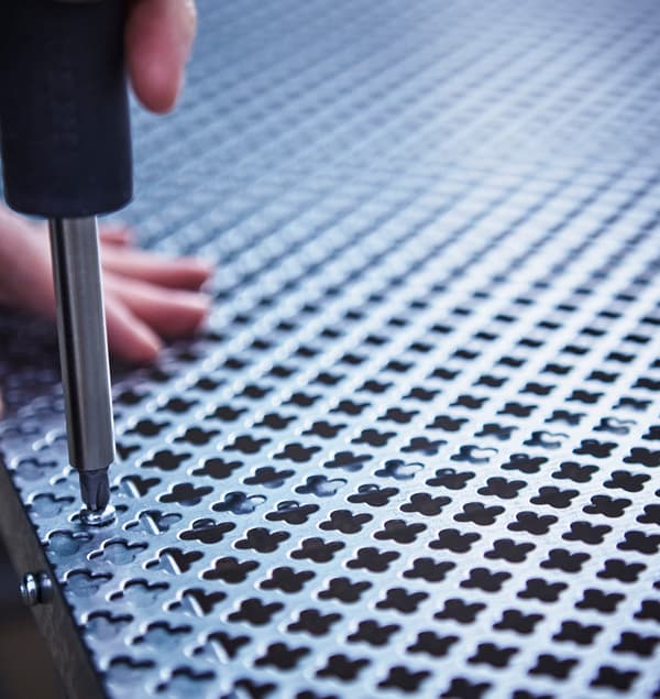 A close-up of a mesh metal sheet being screwed to the back of a IKEA HYLLIS shelving unit.