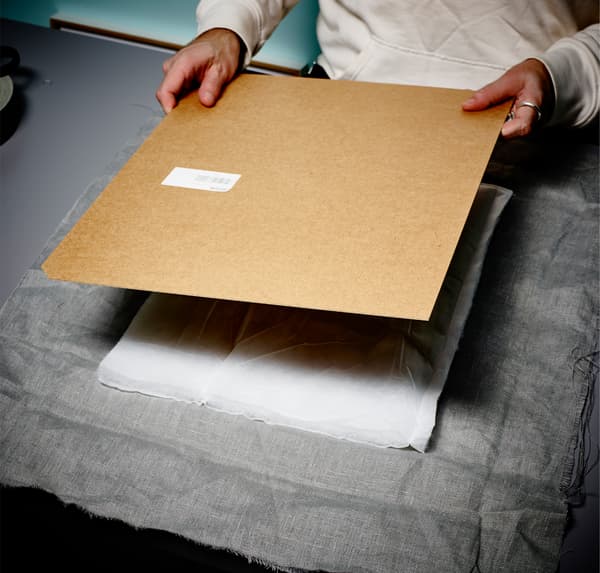 A close up of a person’s hands, layering up grey fabric, white wadding and the back of a photo frame.